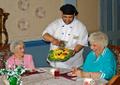 staff member serving fruit to 2 residents in resident's dining room