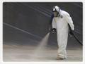 Photo of a worker in a painting suit spraying a roof